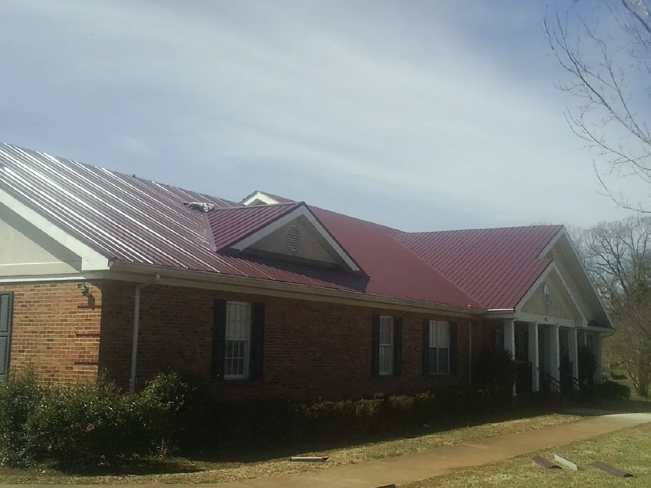 Red metal roof with gabled entries on a long brick building, from a Hail Damage Roof Repair job in Cassatt