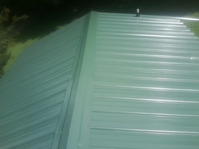 New green metal panels meeting at the ridge of a roof — Flat Roof Repair work by our crew in Cassatt