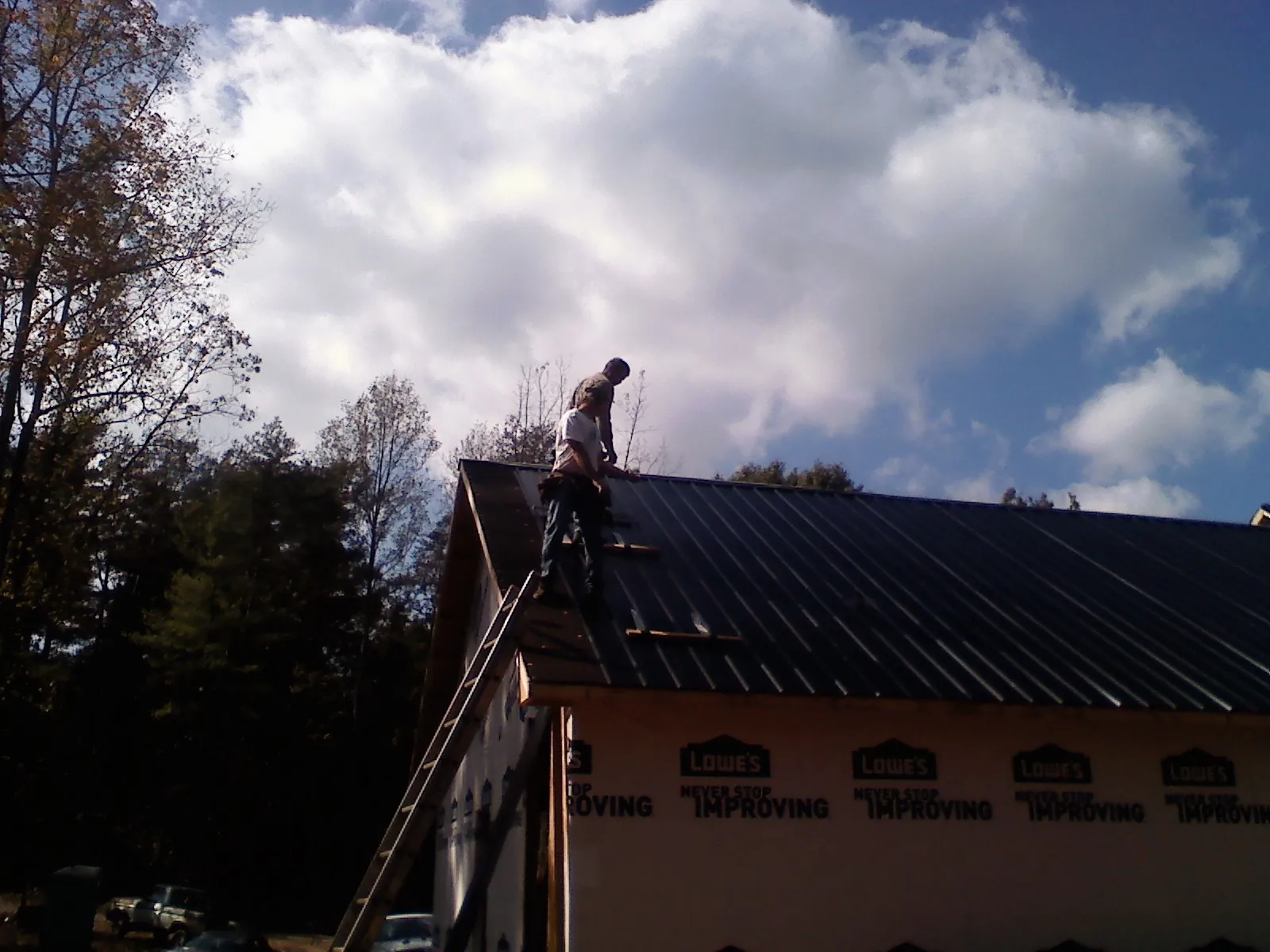 Roofer fastening dark metal panels high against a cloudy sky, from a Roof Inspection job in Cassatt