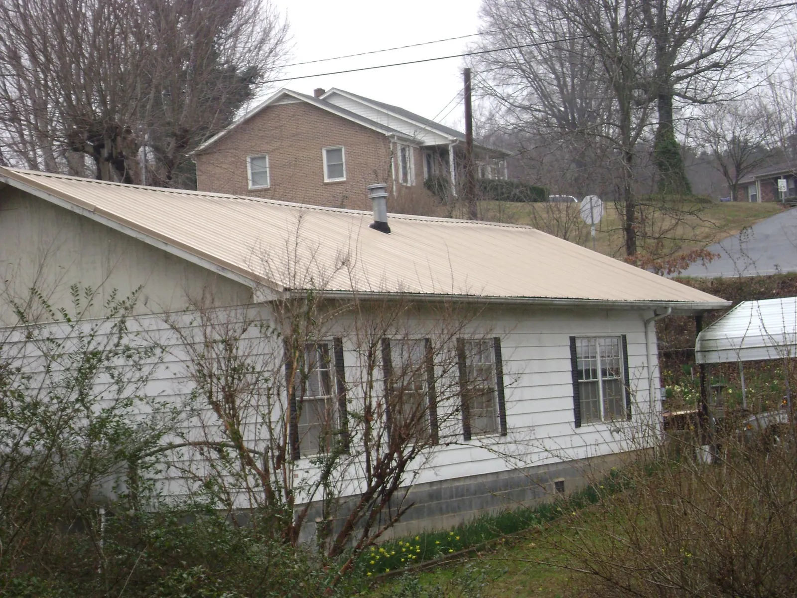 Tan metal roof on a white sided house set into a hillside — Commercial Roofing by Roofing Brothers in Cassatt